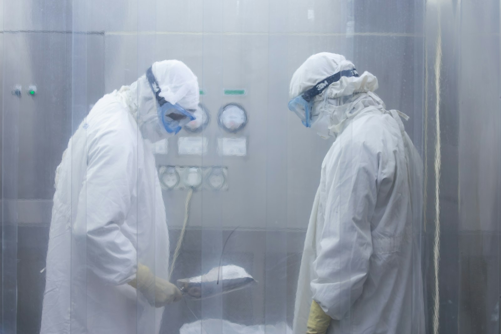 Two operators in protective cleanroom suits working in a controlled room